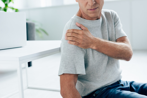 cropped view of man in t-shirt feeling pain in shoulder in apartment  - Zdjęcie, obraz