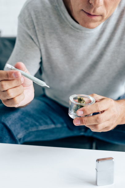 cropped view of man in t-shirt holding blunt and medical marijuana buds - Foto, Imagen