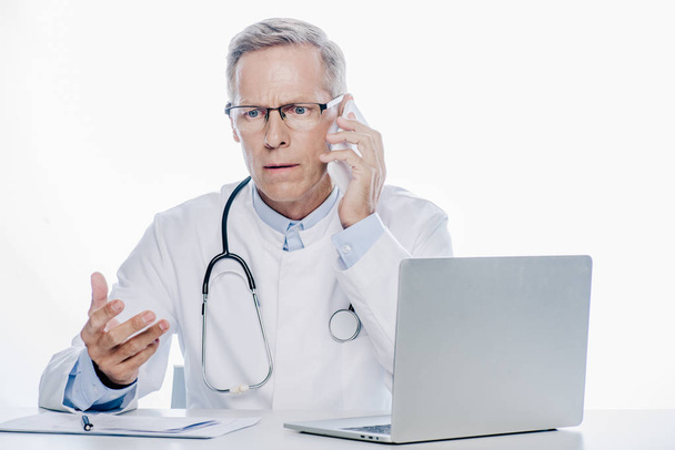 guapo médico de bata blanca hablando en el teléfono inteligente aislado en blanco
 - Foto, Imagen