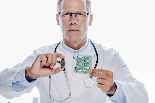 schöner Arzt im weißen Kittel mit medizinischem Marihuana und Tabletten isoliert auf weiß - Foto, Bild