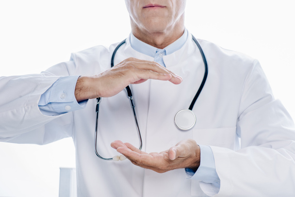 bijgesneden weergave van de arts in witte vacht houden handen geïsoleerd op wit - Foto, afbeelding