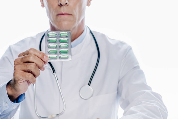 vista recortada del médico de bata blanca sosteniendo píldoras aisladas en blanco
  - Foto, imagen