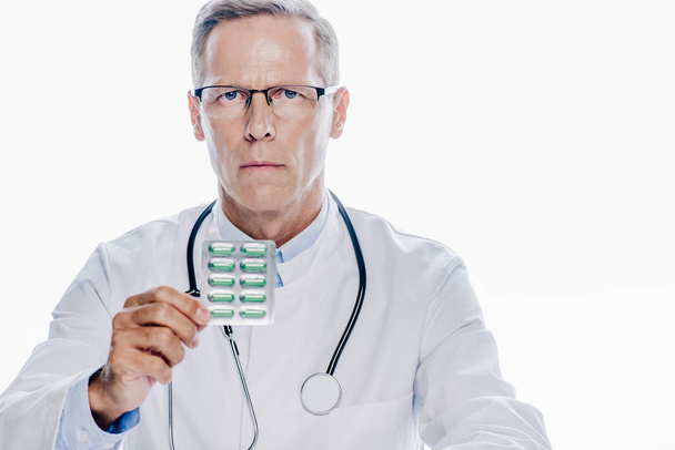 handsome doctor in white coat holding pills isolated on white  - Foto, Imagen