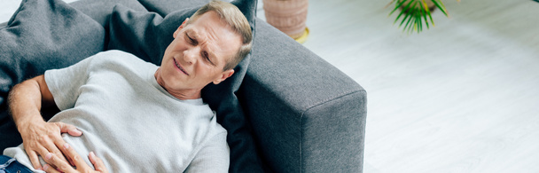 панорамный снимок красивого мужчины с болью в животе в квартире
  - Фото, изображение