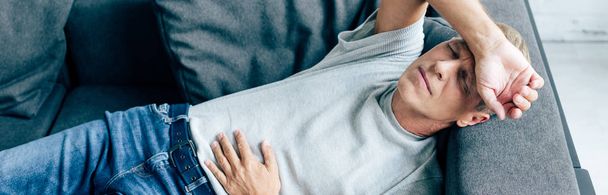 panoramatický záběr krásného muže s bolestí břicha v bytě  - Fotografie, Obrázek