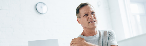 panoramic shot of handsome man feeling pain in shoulder in apartment  - Photo, Image