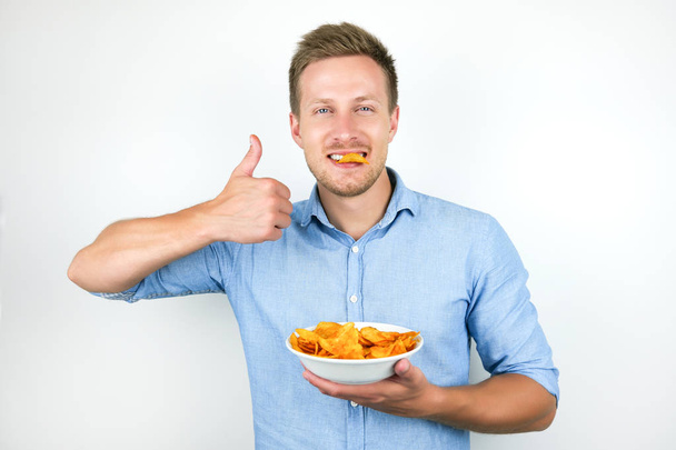 young handsome man holds chips in his mouth showing like sign on isolated white background - Foto, afbeelding