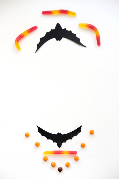 Хэллоуин украшения с летучей мышью, конфеты, сладкие черви на белом фоне. Кошелек или жизнь. Счастливый Хэллоуин. Копирование пространства
 - Фото, изображение