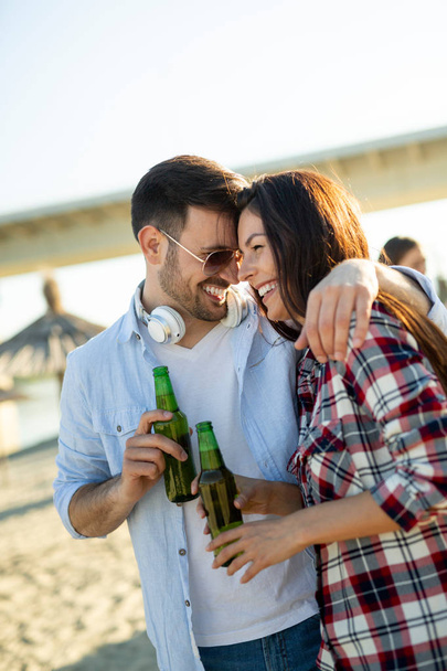 Joyeux jeune couple souriant et buvant de la bière à la plage - Photo, image