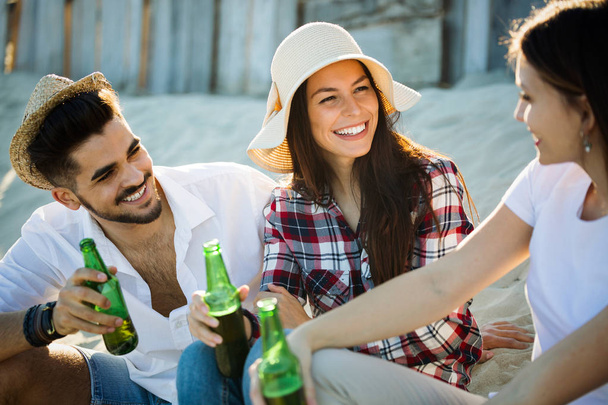 Grupo de jovens amigos rindo e bebendo cerveja na praia
 - Foto, Imagem
