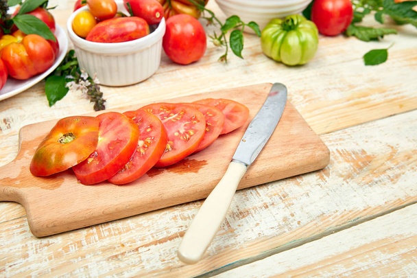 Chopped tomatoes and knife on cutting board. Mix of tomatoes background. Beautiful juicy organic red tomatoes on white wooden table background. Clean eating concept. Copy space, flat lay. - Fotó, kép