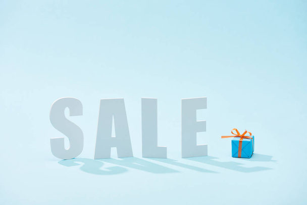 white sale lettering and festive gift box on blue background - Φωτογραφία, εικόνα