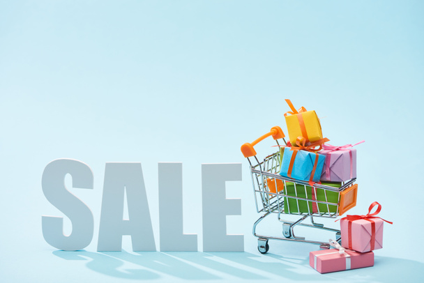 white sale lettering and festive gift boxes in shopping cart on blue background - Valokuva, kuva