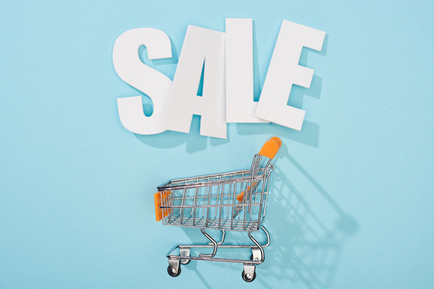 top view of white sale lettering and empty shopping cart on blue background - Photo, image