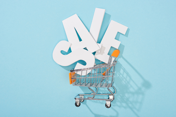 top view of white sale lettering in decorative shopping cart on blue background - Foto, afbeelding