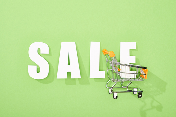 top view of white sale lettering and shopping cart on green background - Foto, immagini