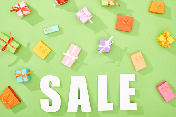 top view of scattered decorative gift boxes and shopping bags on green background with sale word - Photo, Image