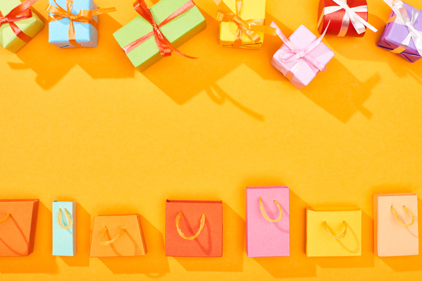 Top uitzicht van feestelijke verpakt geschenken en boodschappentassen op heldere oranje achtergrond - Foto, afbeelding