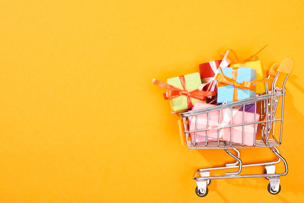 top view of shopping cart with presents on bright orange background - Fotoğraf, Görsel