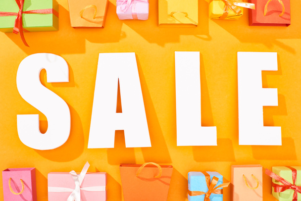 top view of white sale lettering near shopping bags and presents on bright orange background - Φωτογραφία, εικόνα