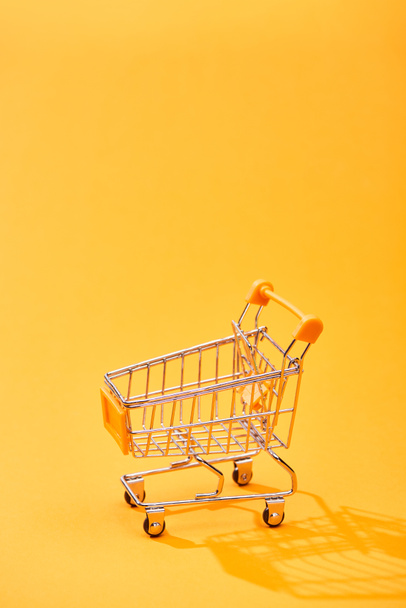 empty small shopping cart on bright orange background - Foto, afbeelding