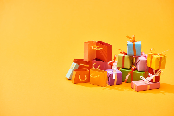 πολύχρωμα τυλιγμένο εορταστικά δώρα με σακούλες για ψώνια σε φωτεινό πορτοκαλί φόντο - Φωτογραφία, εικόνα