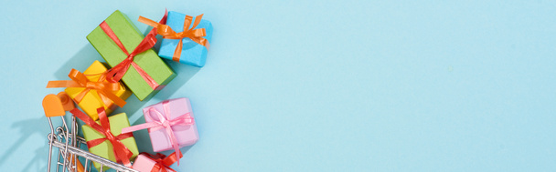 Top uitzicht van kleurrijke feestelijke geschenkdozen in winkelwagen op blauwe achtergrond, panoramische foto - Foto, afbeelding