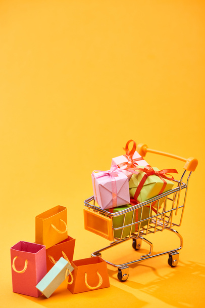 shopping cart with presents near shopping bags on bright orange background - Foto, Imagem