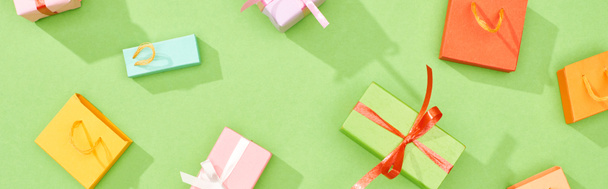 panoramische foto van verspreide geschenkdozen en boodschappentassen op groene achtergrond - Foto, afbeelding