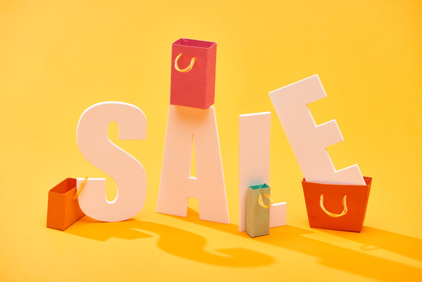 white sale lettering with shopping bags on bright orange background - Foto, afbeelding