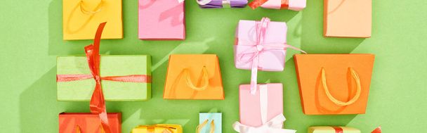 platte lay met kleurrijke geschenkdozen en boodschappentassen op groene achtergrond, panoramische foto - Foto, afbeelding