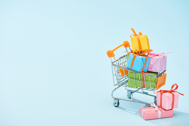 festive wrapped presents in shopping cart on blue background with copy space - Fotoğraf, Görsel