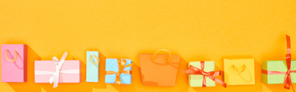 πανοραμική φωτογραφία σακούλες για ψώνια και τυλιγμένο δώρα σε φωτεινό πορτοκαλί φόντο - Φωτογραφία, εικόνα