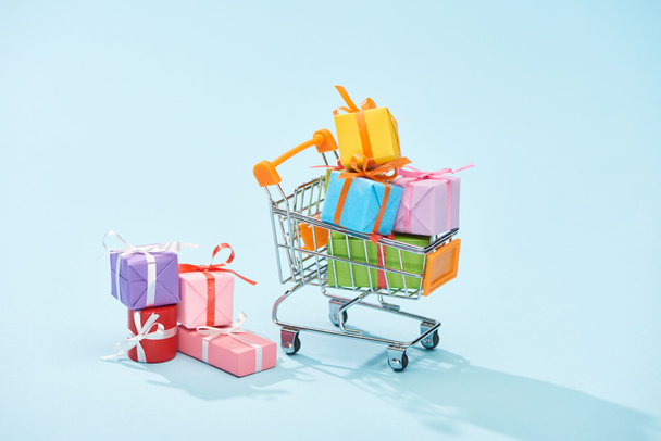festive wrapped gifts in shopping cart on blue background - 写真・画像