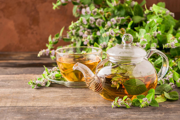 カップにレモンバームミントの新鮮な葉と木製の素朴な背景にティーポットとお茶。ヒーリングハーブドリンク. - 写真・画像