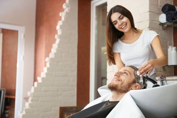 Female hairdresser washing hair of young man in salon - Photo, Image