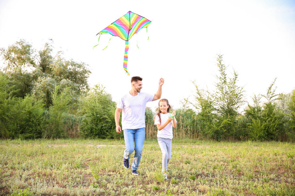 Young man with little daughter flying kite outdoors - Foto, Bild