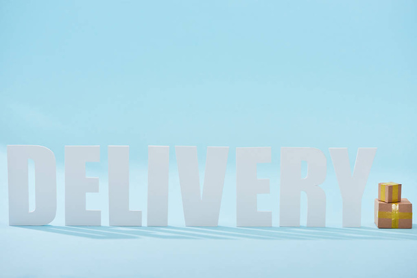 біле слово доставки поблизу закритих картонних коробок на синьому фоні з пробілом для копіювання
 - Фото, зображення