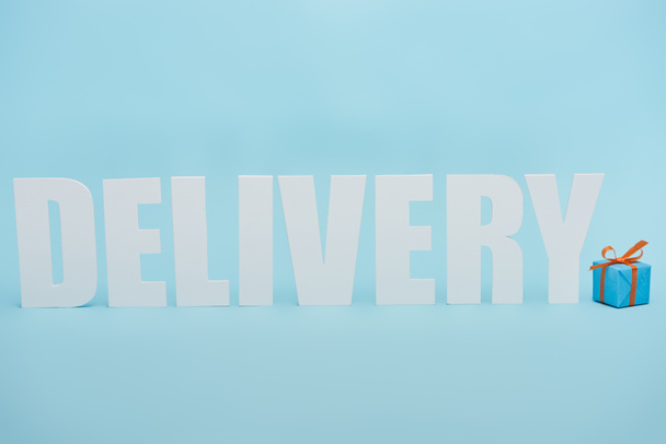 white delivery inscription with shadows near gift box on blue background - Фото, изображение