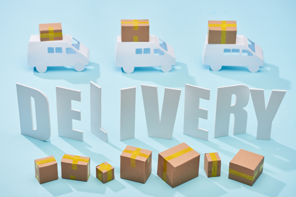 white delivery inscription between mini trucks and closed cardboard boxes on blue background - Фото, зображення