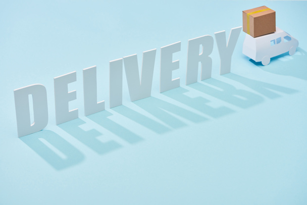 delivery inscription near white mini truck with cardboard box on blue background - Foto, immagini