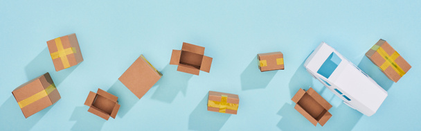 Foto panorámica de paquetes de cartón cerrados y abiertos cerca de mini furgoneta sobre fondo azul
 - Foto, imagen