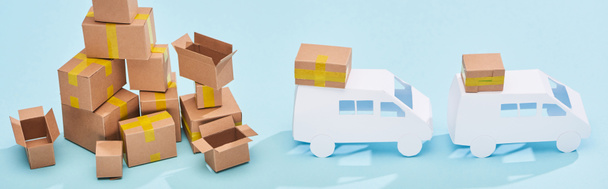 plano panorámico de pila de cajas de cartón cerca de mini camiones sobre fondo azul
 - Foto, imagen