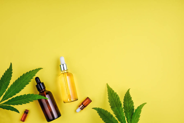 Bottles with CBD oil, a dropper, and leaf marijuana on yellow background. Concept beauty care with hemp oil - Photo, Image