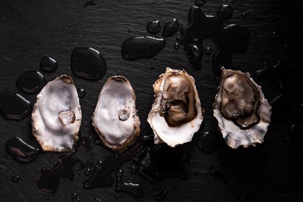 Opened fresh oysters on a dark background and water drops. - Photo, Image