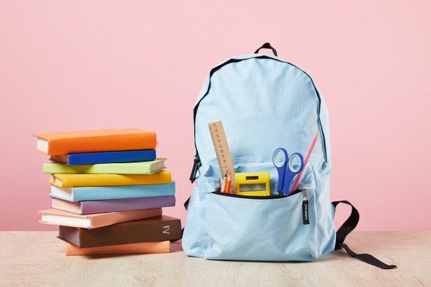 escola mochila azul com suprimentos no bolso perto de livros isolados em rosa
 - Foto, Imagem