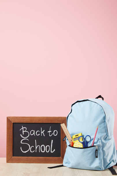 黒板の近くにポケットに消耗品が入った青いバックパックと、ピンクに孤立した学校の文字に戻る - 写真・画像