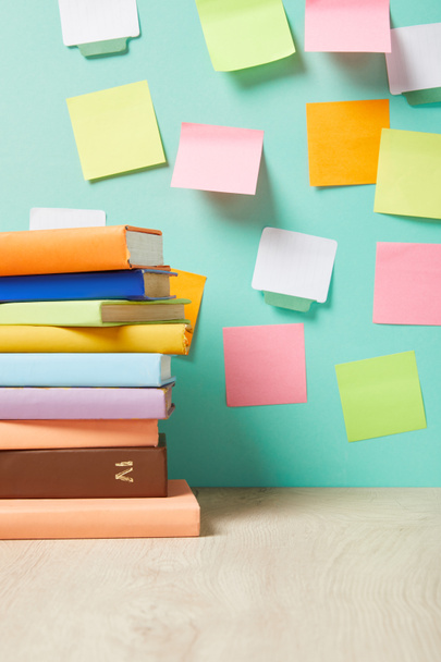 stack of books on table near multicolored sticky notes on turquoise wall - Photo, Image