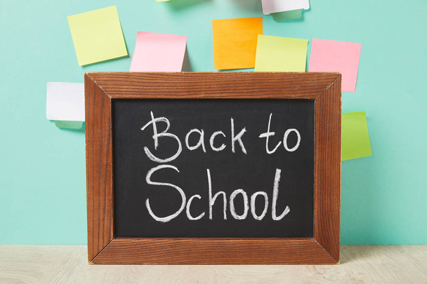 chalkboard with back to school lettering near multicolored sticky notes on turquoise wall - Photo, Image