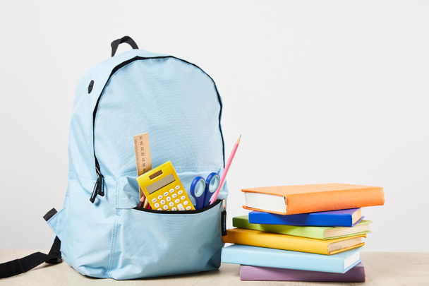 blue backpack with school supplies near books isolated on white - Foto, afbeelding